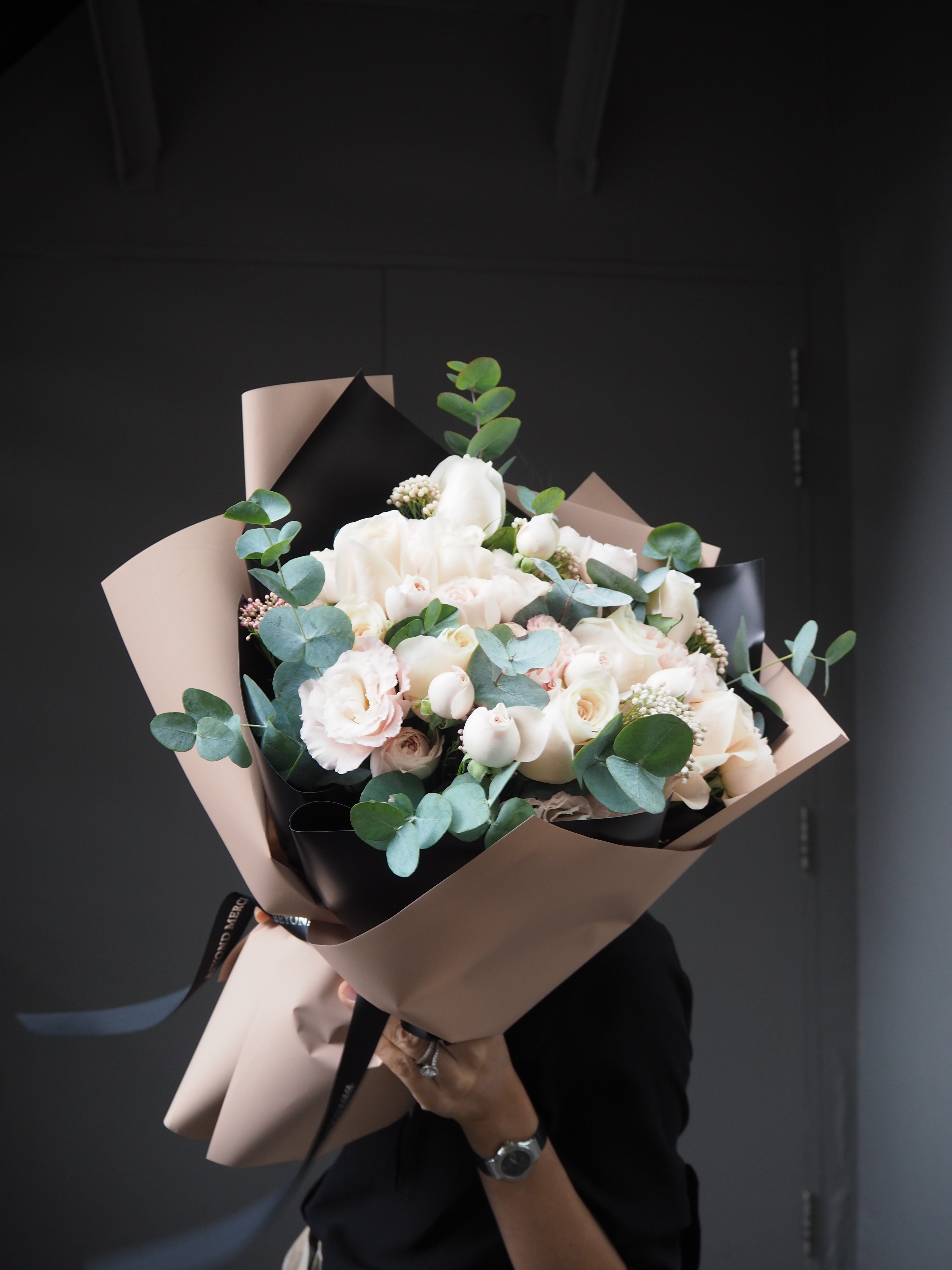 Bouquet of white flowers in brown paper packaging on a dark surface