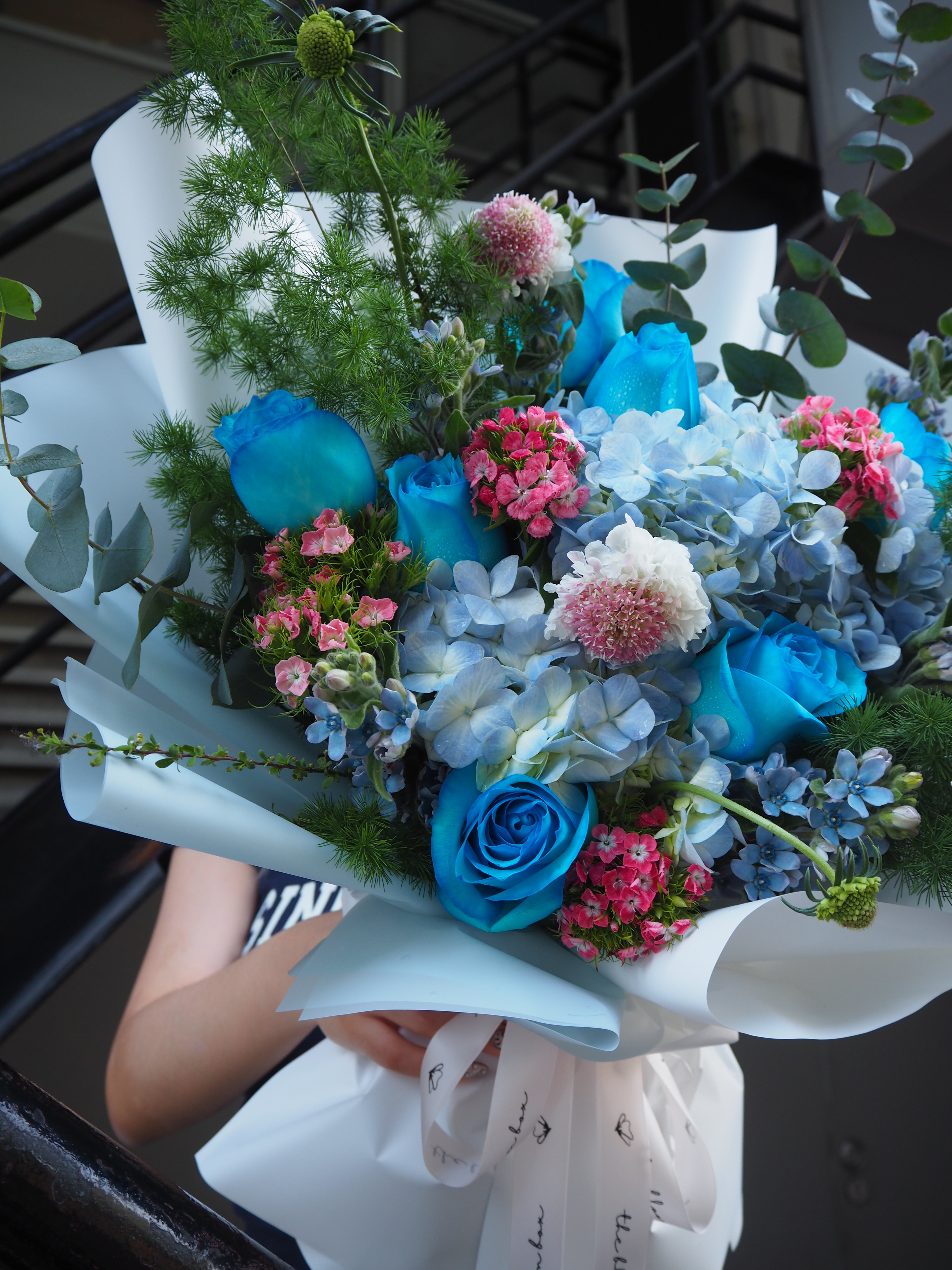 Luxury fresh flower bouquet of blue and pink flowers with greenery held by a person.