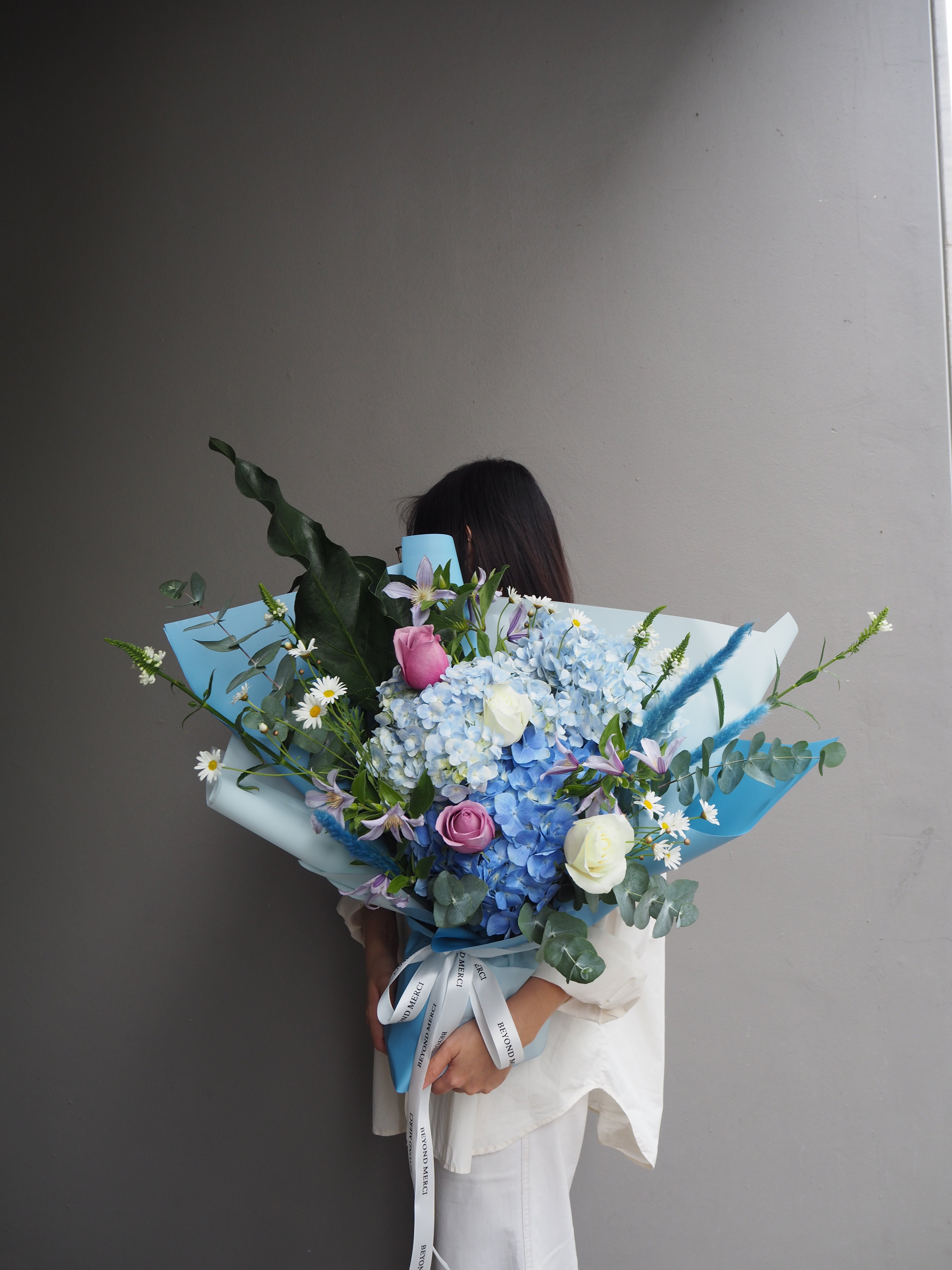 Model holding a fresh luxury bouquet of flowers with hydrangeas, purple rose and green foliage.