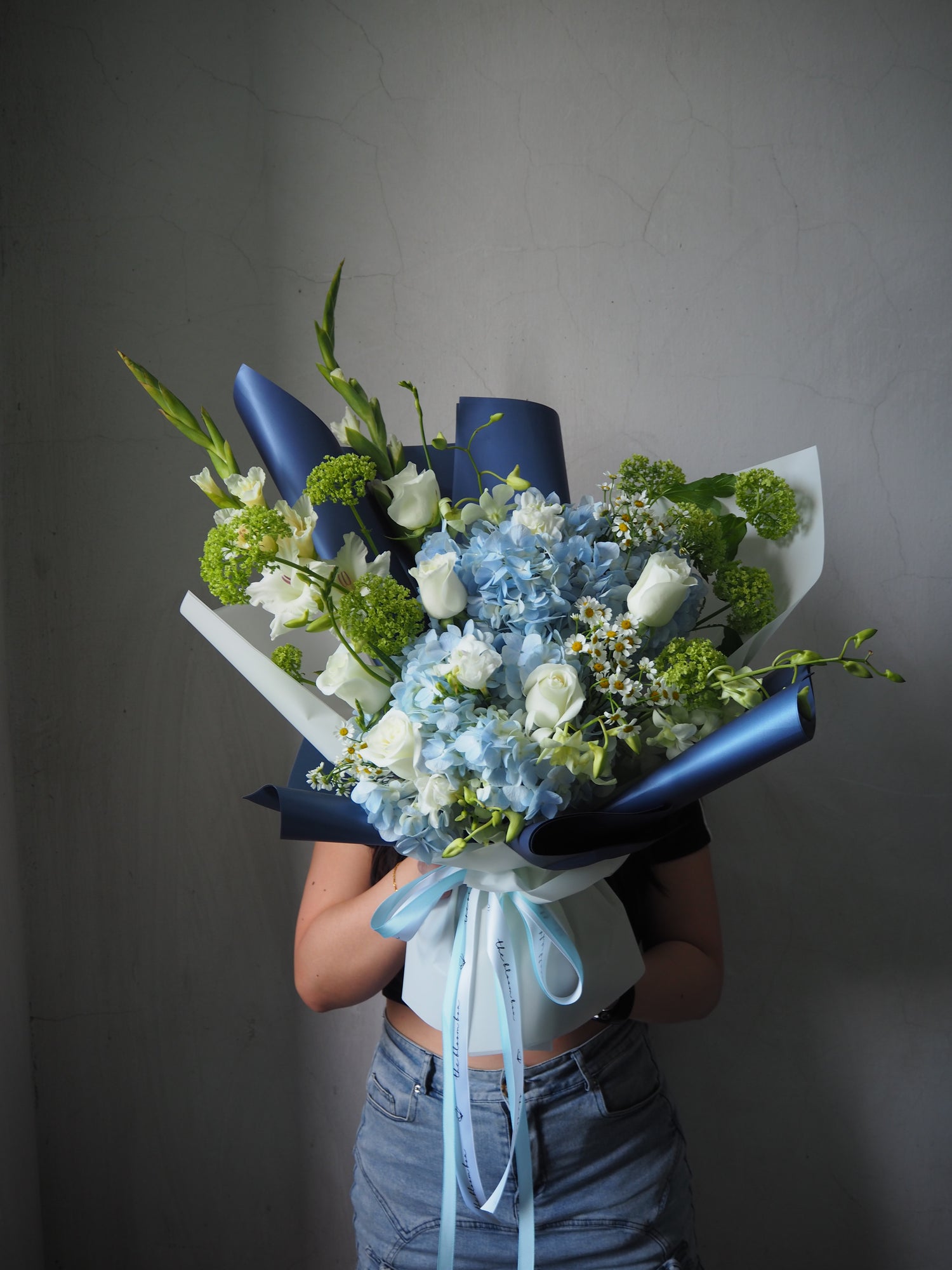 Bouquet of flowers with blue ribbons held against a plain background