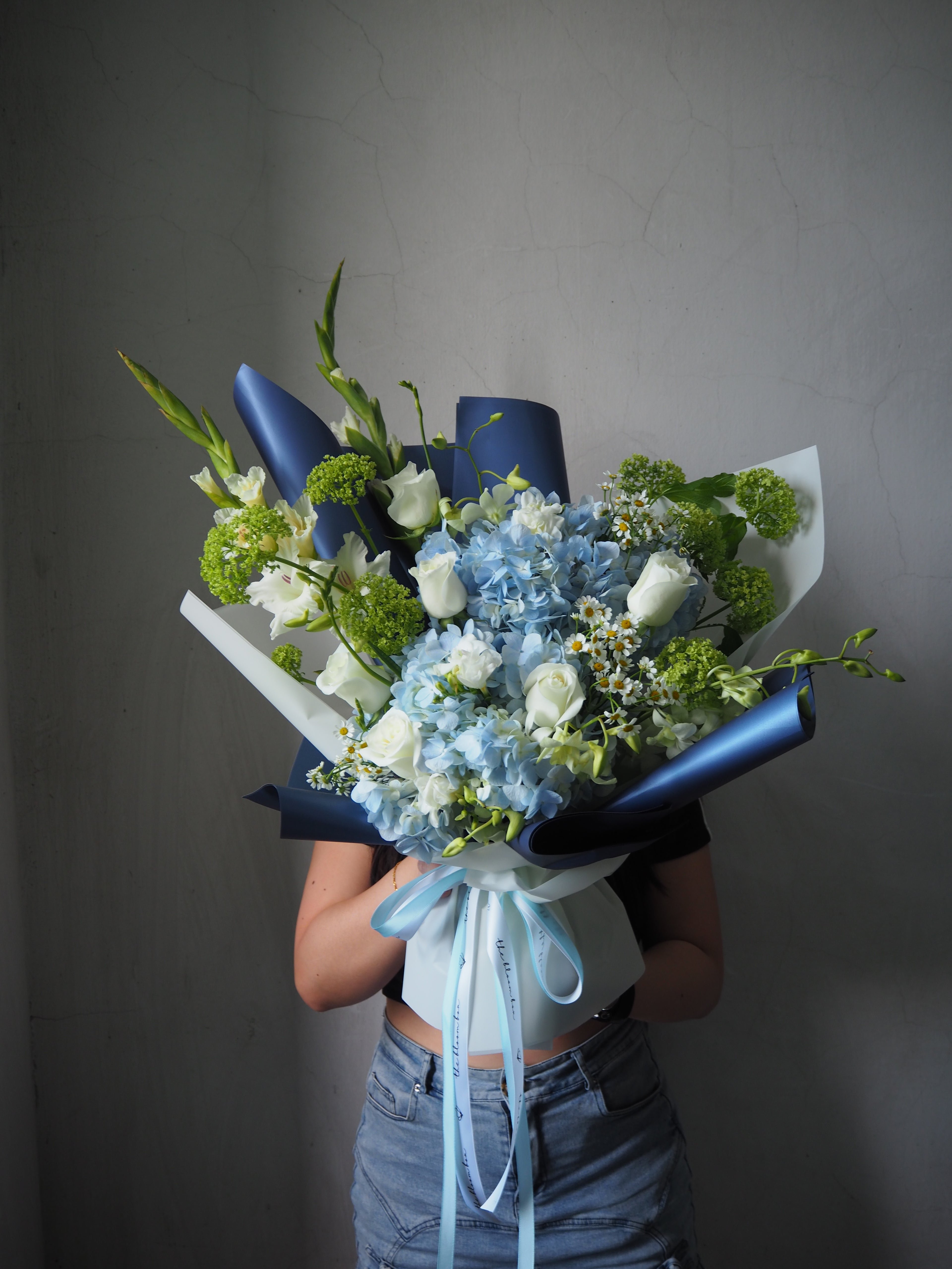 Bouquet of flowers with blue ribbons held against a plain background