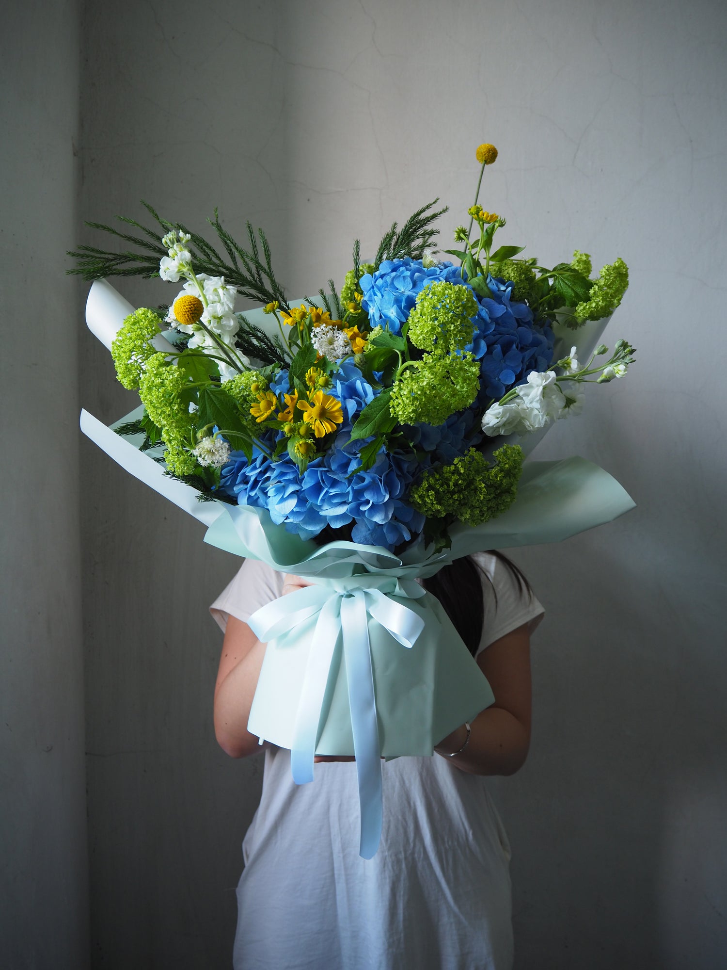 Person holding a bouquet of flowers with blue and green colors against a plain background