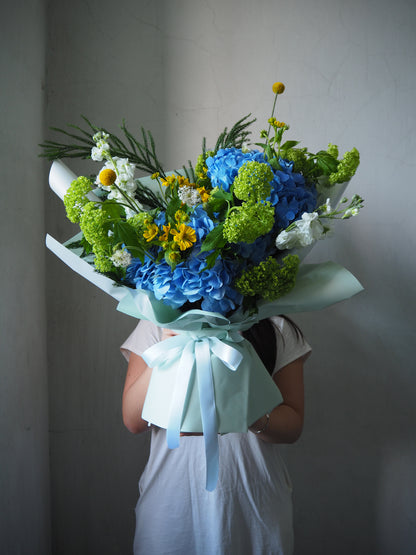 Person holding a bouquet of flowers with blue and green colors against a plain background
