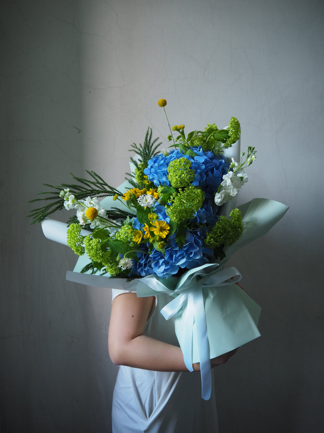 Person holding a bouquet of blue and green flowers against a plain background