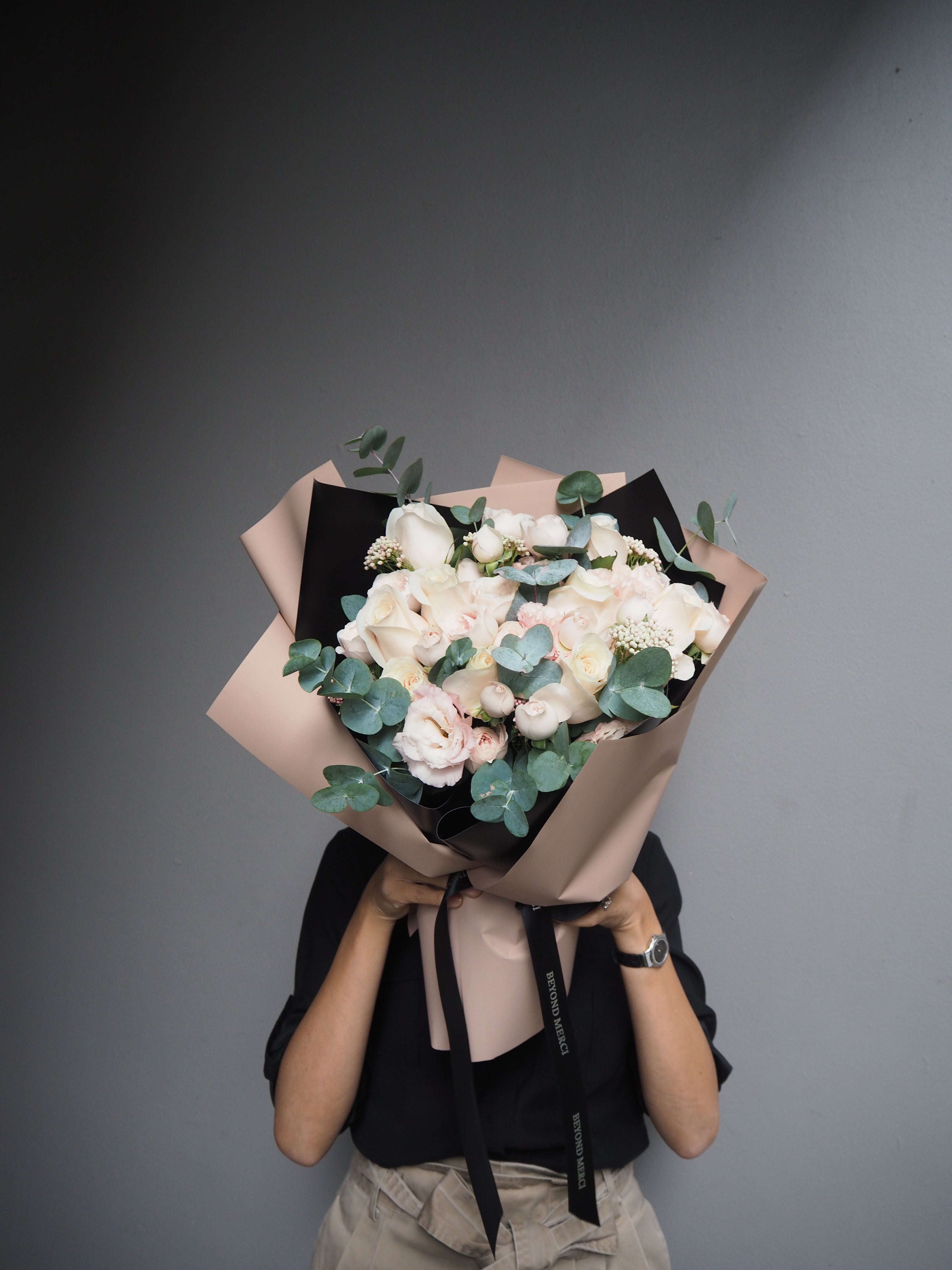 Person holding a fresh bouquet of mix flowers with pale pink rose, eustomas, rice flower.