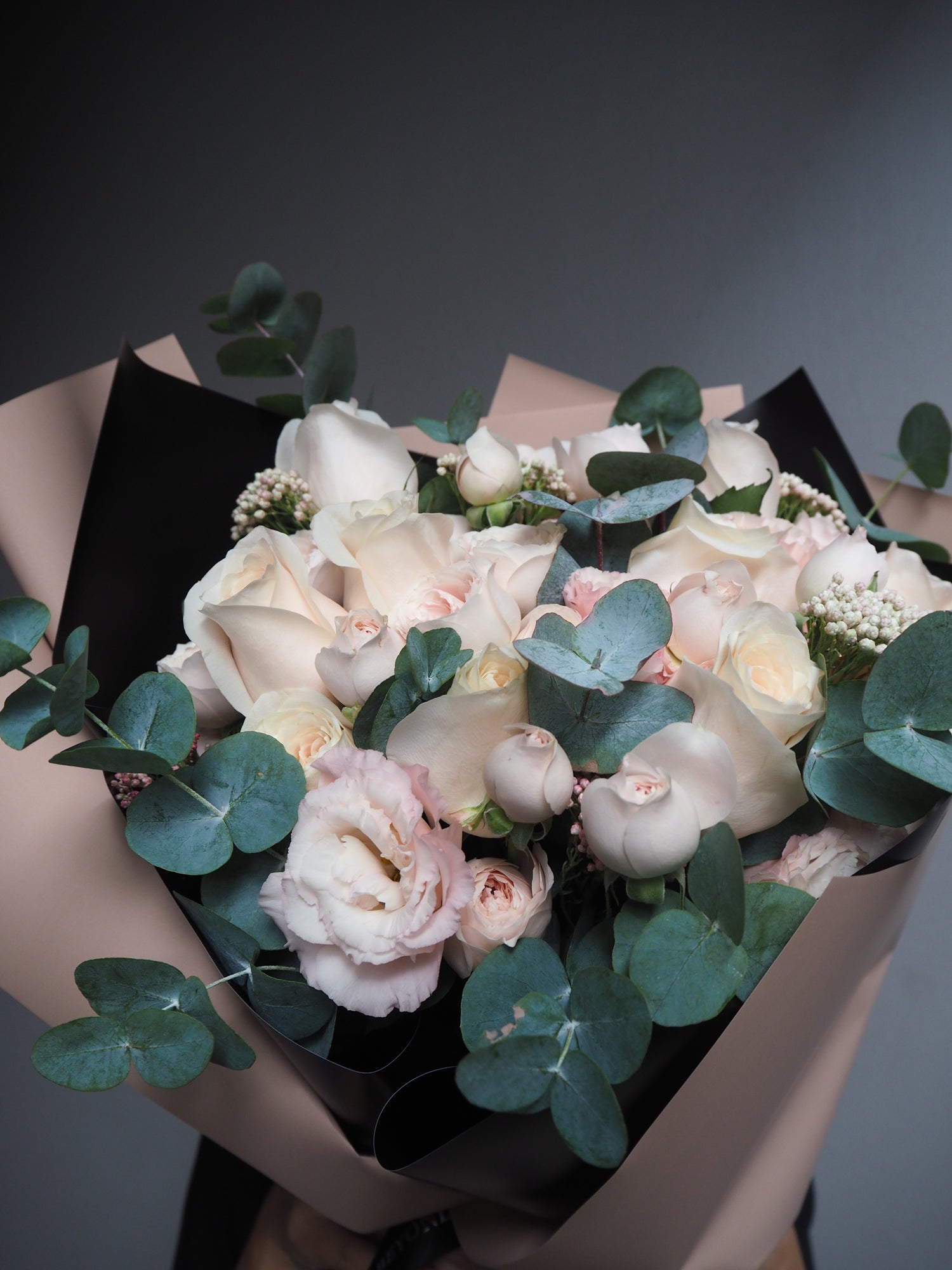 Bouquet of pale pink roses with greenery in brown paper packaging.
