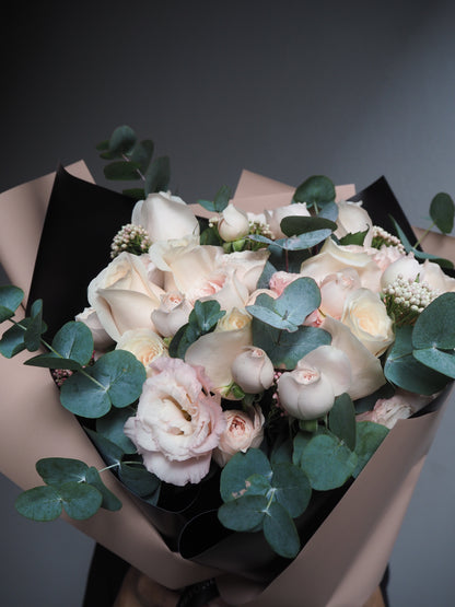 Bouquet of pale pink roses with greenery in brown paper packaging.