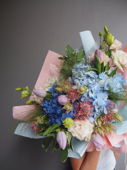 Large premium bouquet of two-tone blue hydrangea and pink tulips flowers with a pink paper wrap on a gray background