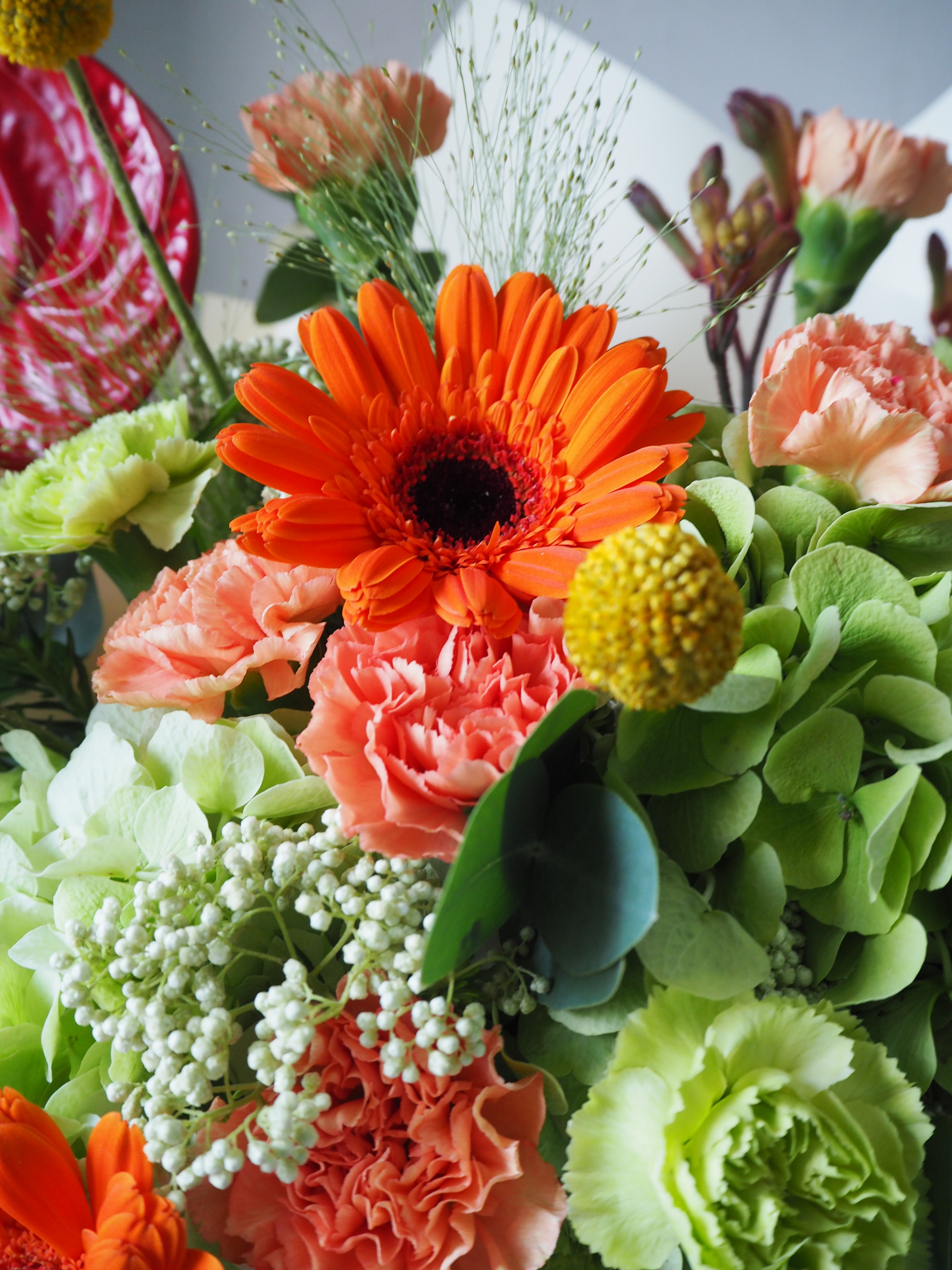 Bouquet of colorful flowers including an orange daisy and green leaves.
