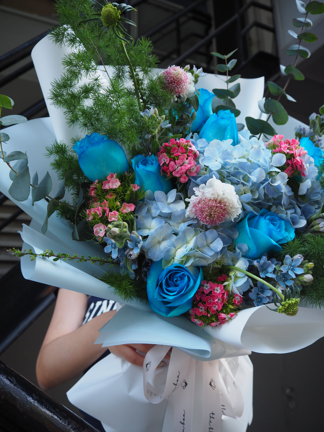 Luxury fresh flower bouquet of blue and pink flowers with greenery held by a person.