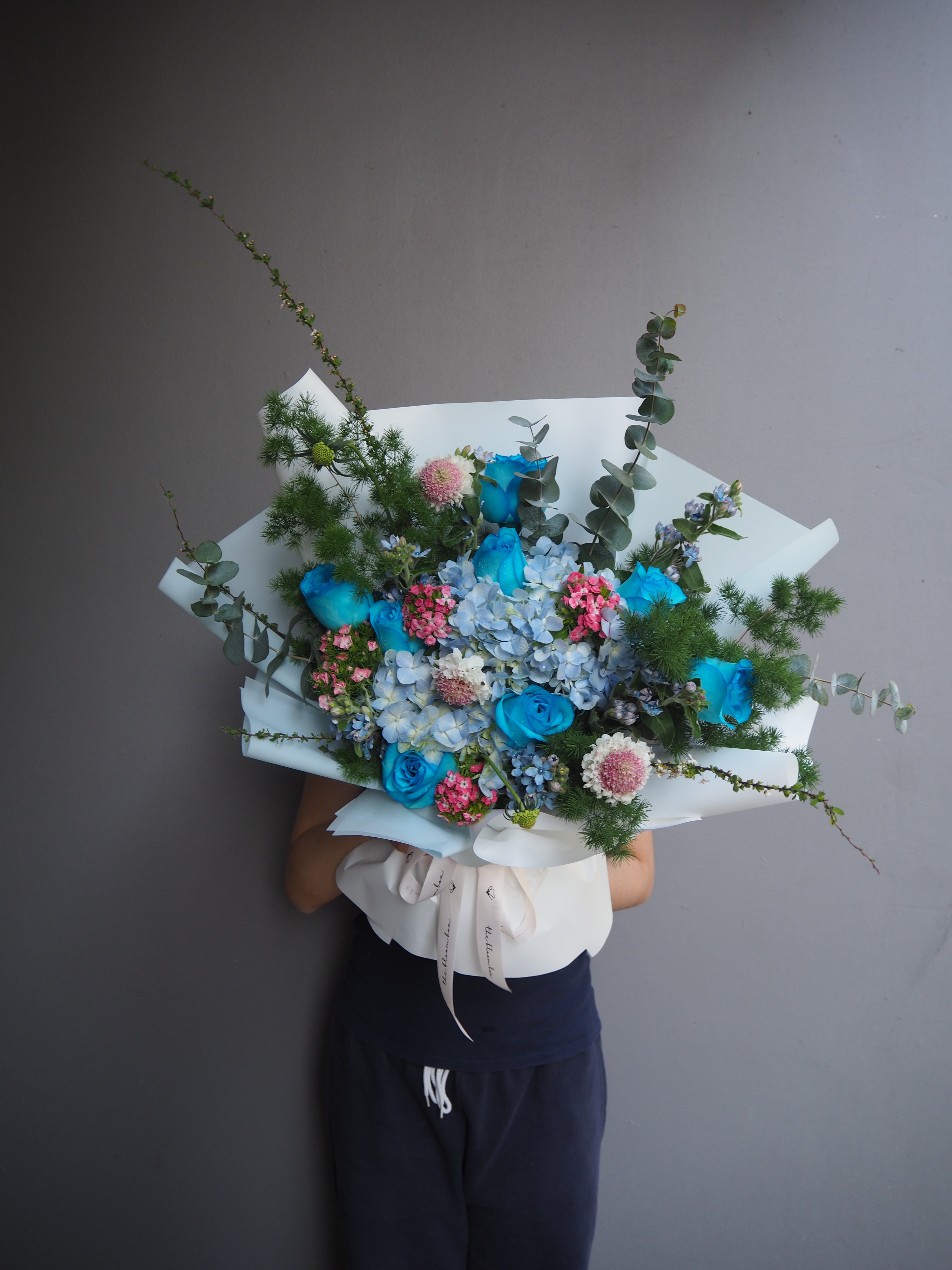 Premium bouquet of blue and pink fresh flowers held by a person against a gray background