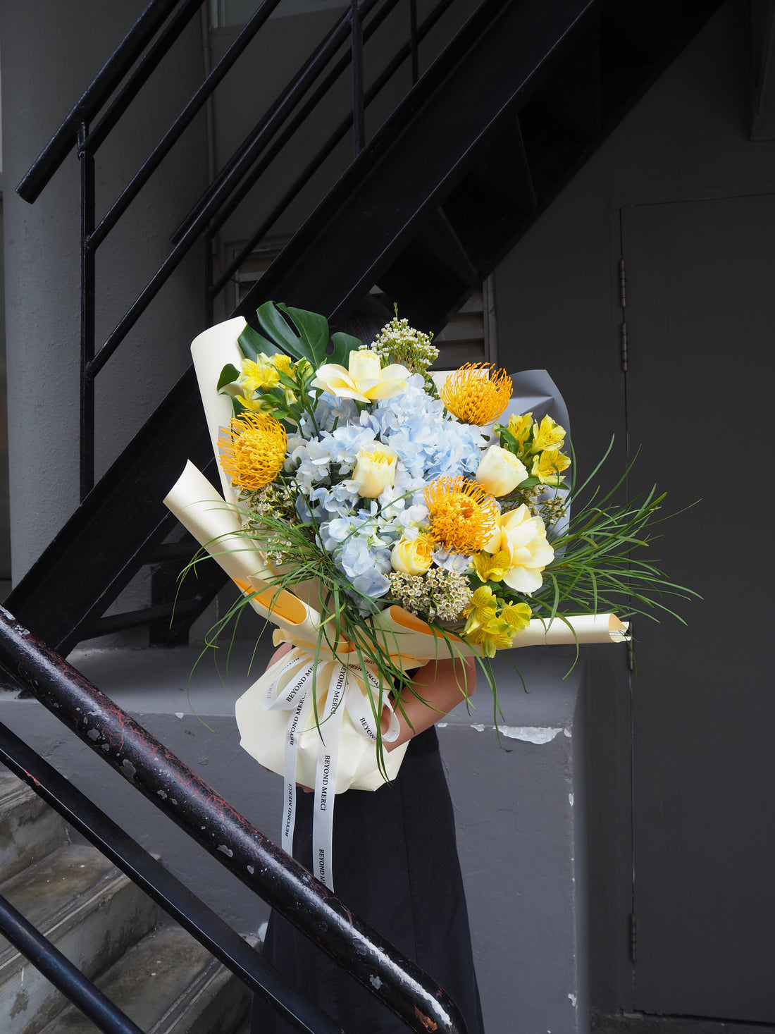 Grand fresh flower bouquet with a mix of pale blue hydrangea, yellow buttercup rose, pin cushion and green foliage.