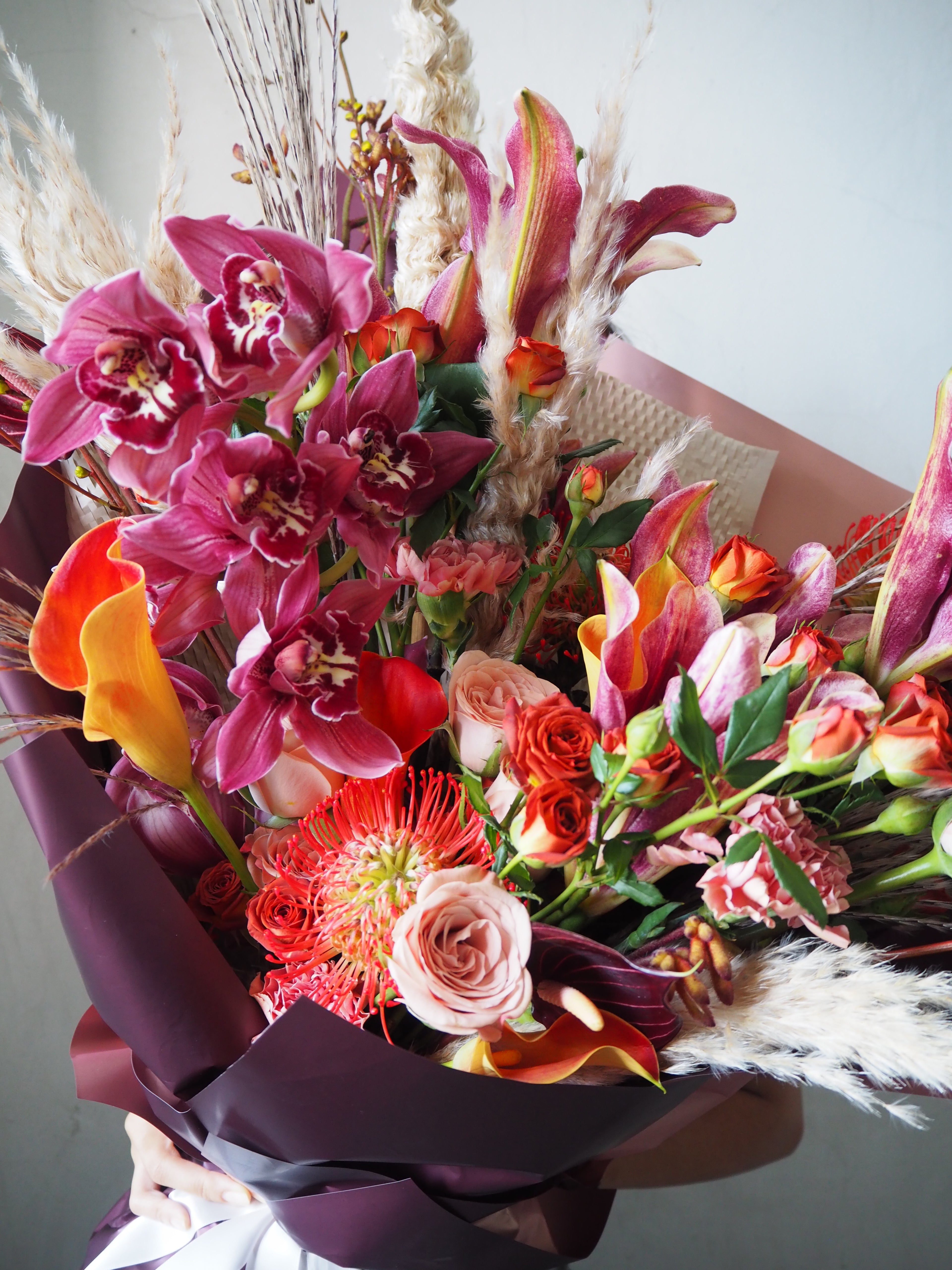 Colorful bouquet of flowers with pink lilies, orange callas, and red roses on a neutral background.