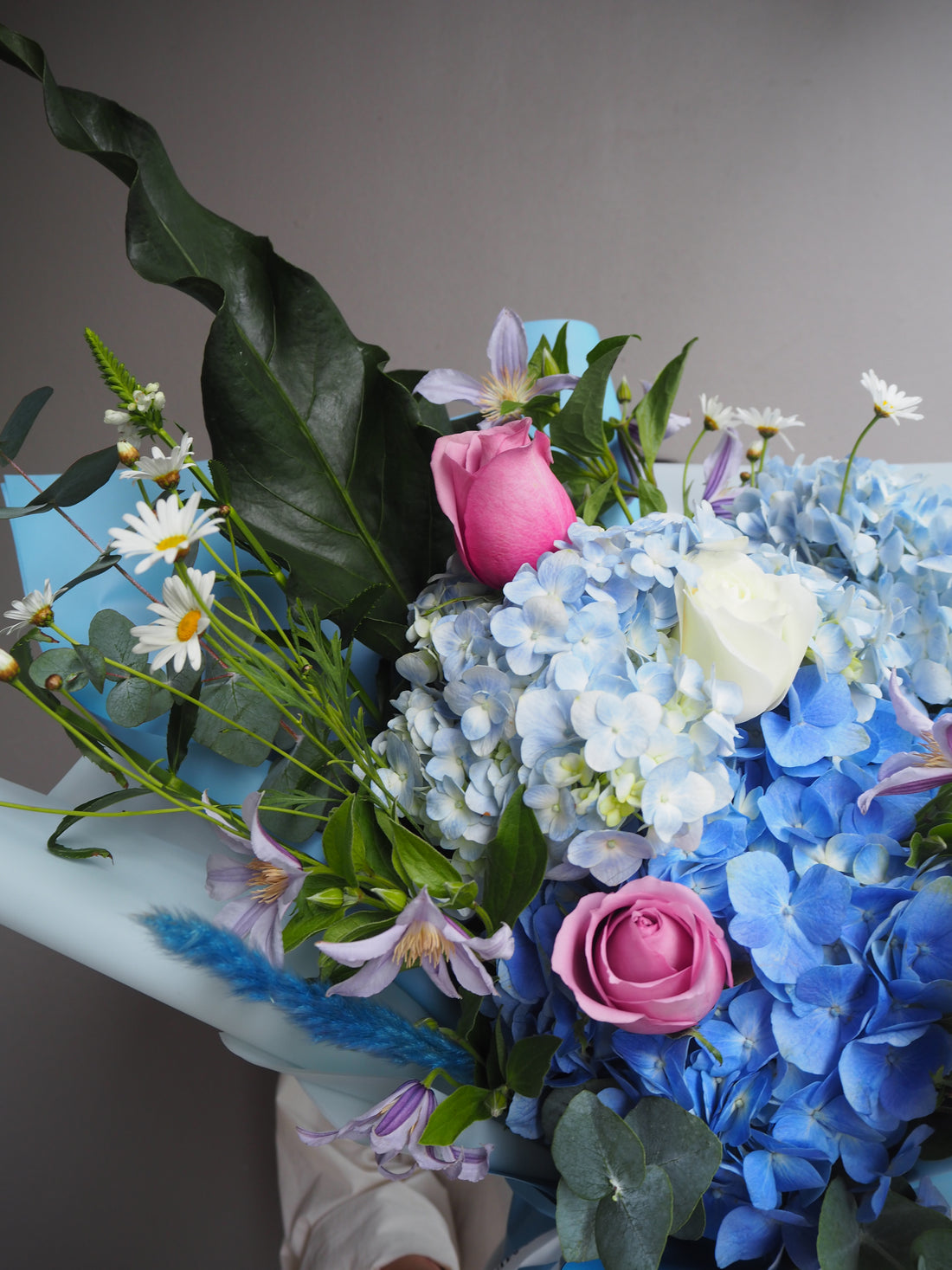 Large bouquet of blue hydrangeas, pink roses, and white daisies in a pale blue wrapper.