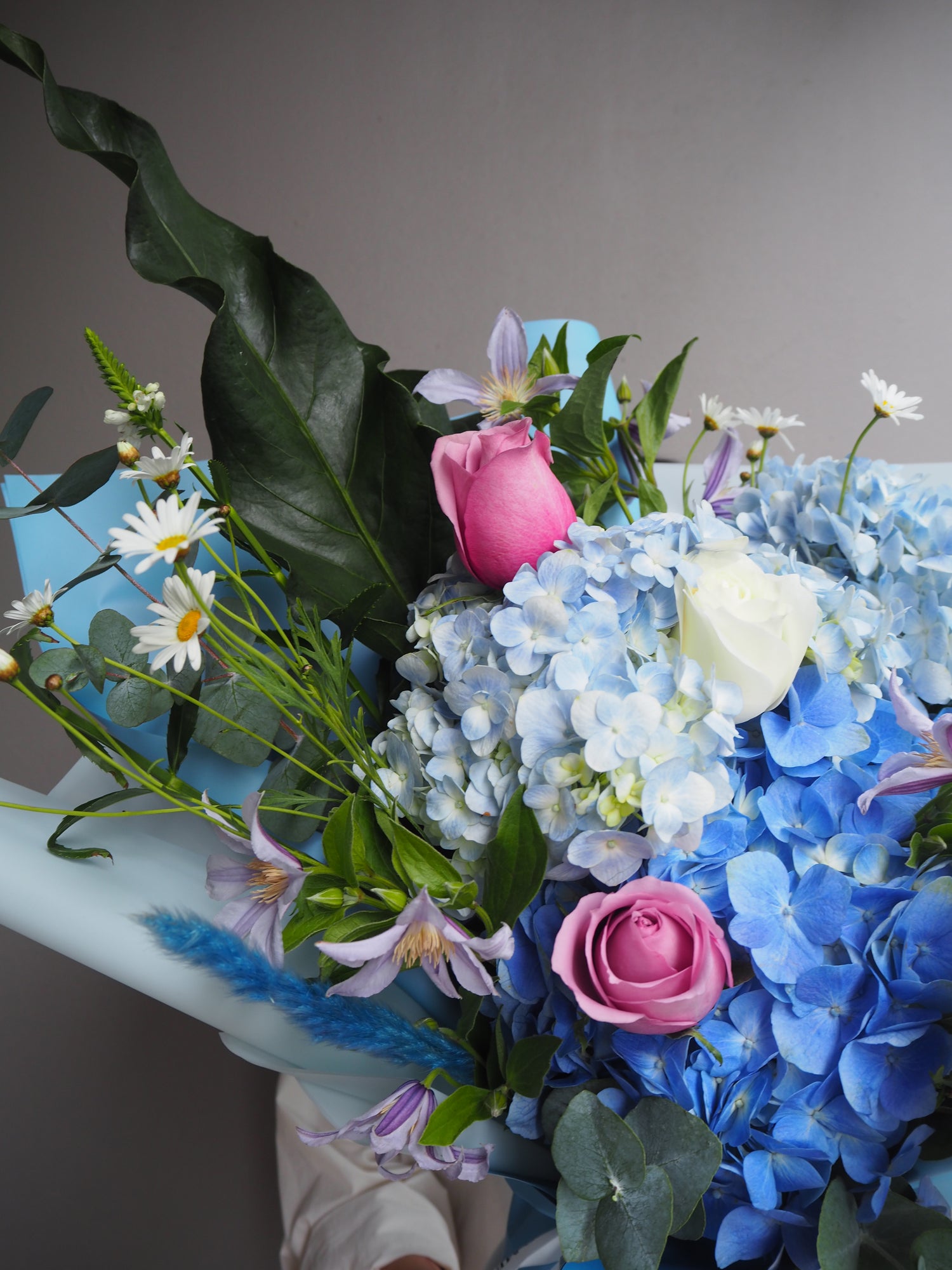 Large bouquet of blue hydrangeas, pink roses, and white daisies in a pale blue wrapper.
